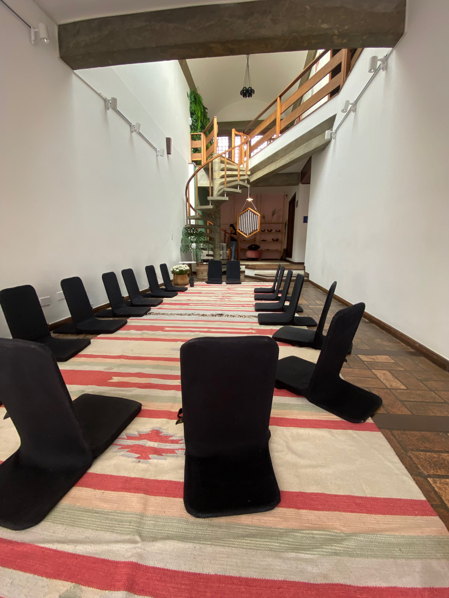 Sala da Casa Magdala preparada em roda com cadeiras de meditação sobre tapete listrado